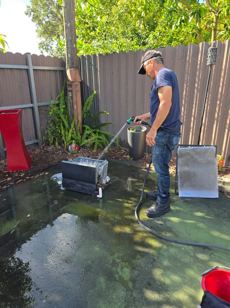 Technician washing an AC condenser coil with water